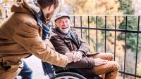 Man sits in wheelchair, and laughs while he speaks with a friend
